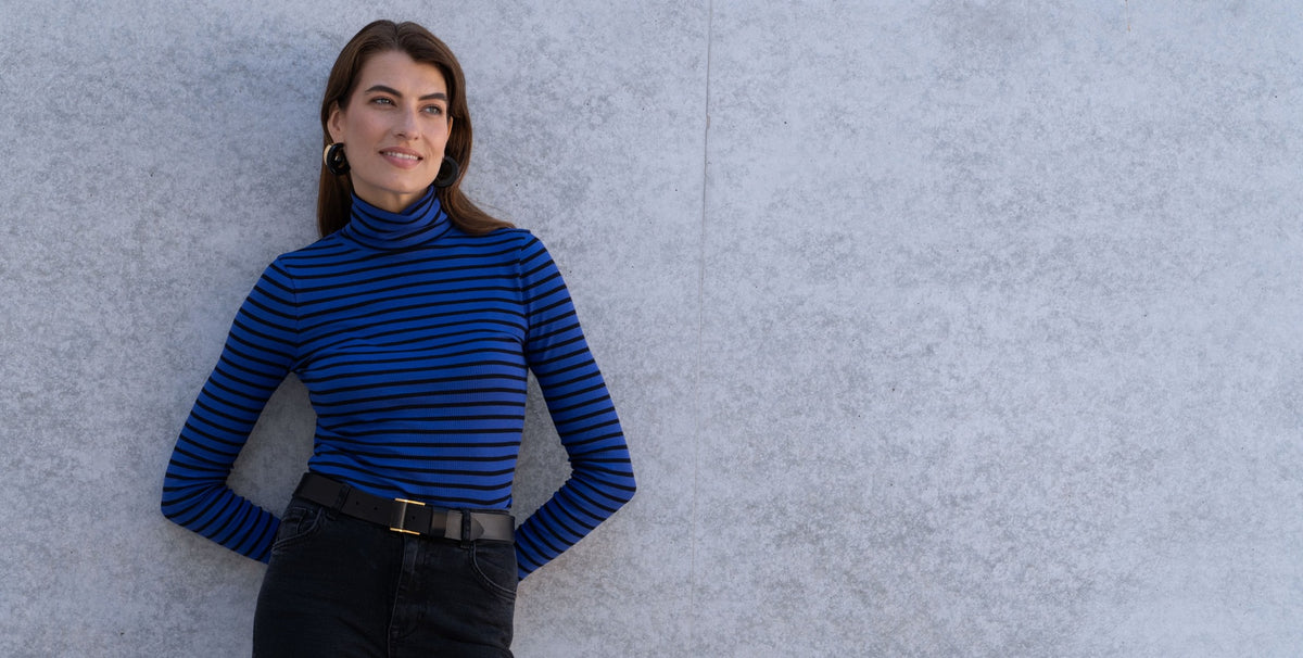 Woman in a blue and black Striped Cotton Roll Neck leaning against a concrete wall